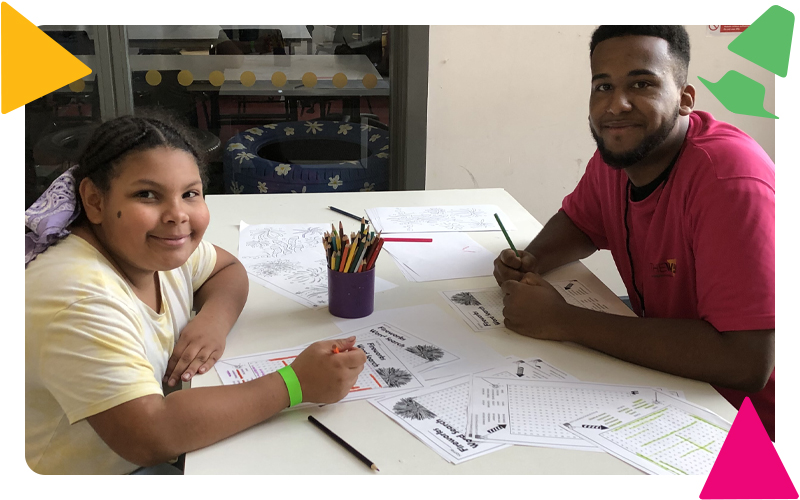 A youth worker and a young girl sitting doing word searches together in the recreation area