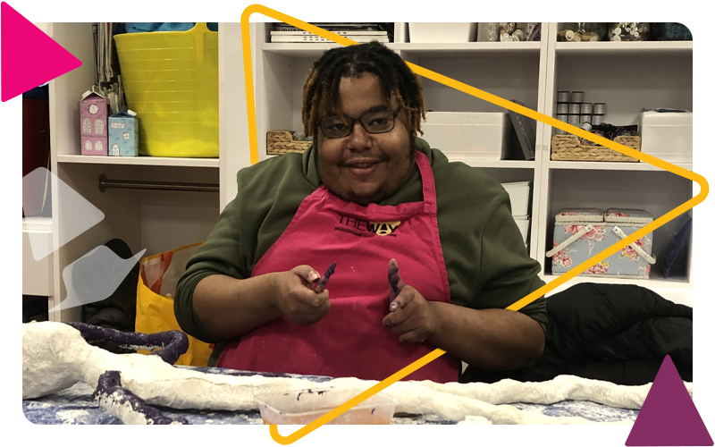 A teenager wearing an apron and working on a sculpture in the art room