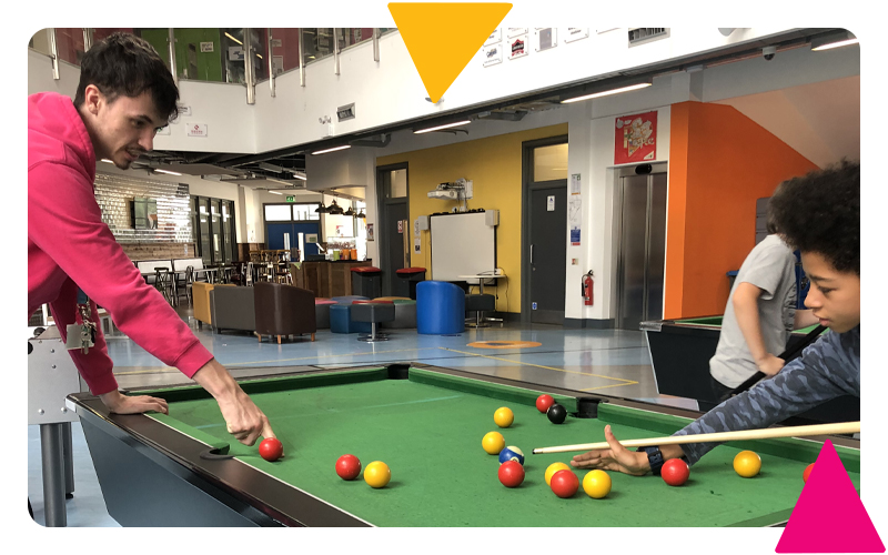 A young boy being coached by a youth worker to play pool