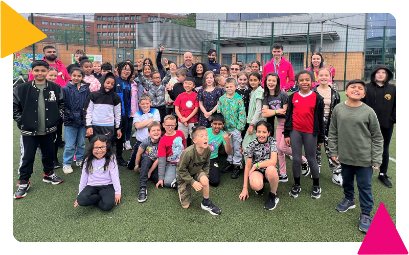 A large group of young people and youth workers smiling on the MUGA pitch