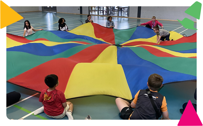 A group of boys and girls with a youth worker, sitting on the floor, playing with a brightly coloured parachute