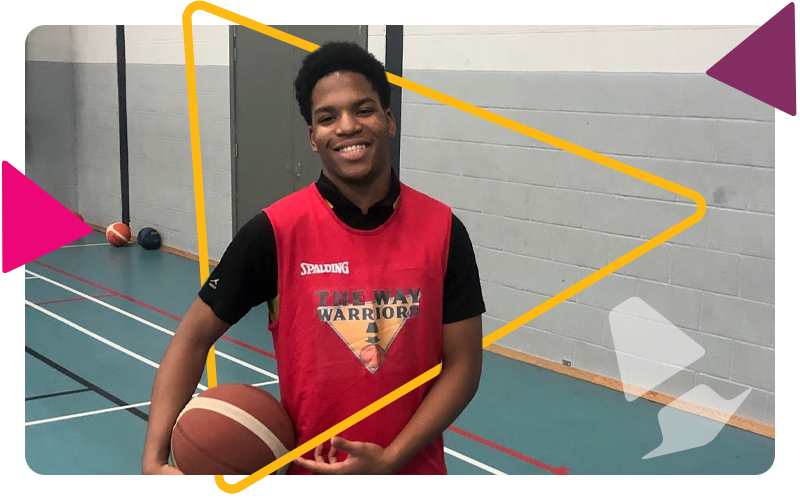 A teenage boy in the sports hall, wearing a sports bib and holding a basketball ball