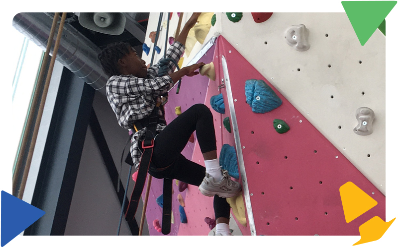 A young girl climbing up a rock climbing wall, wearing a harness