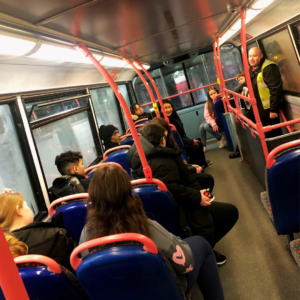 Eight young people and two grown-ups sitting in a bus and a bus driver talking to them