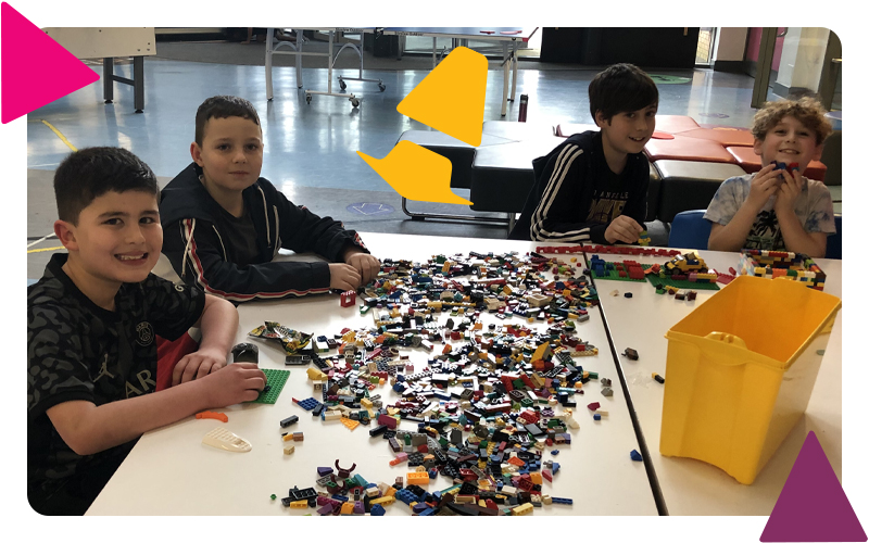 Four boys sitting together, smiling and playing with lego on a large white table