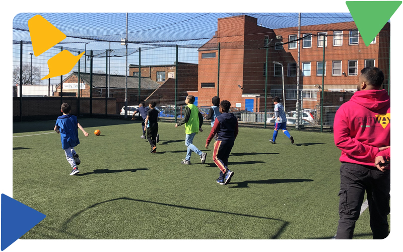 A group of boys on the MUGA pitch playing football in the sunshine