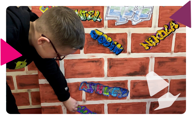 A young boy sticking his grafitti style name tag onto a painted brick wall