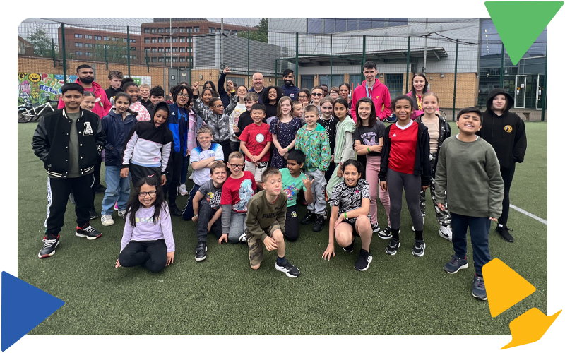 A large group of young people and youth workers smiling on the MUGA pitch