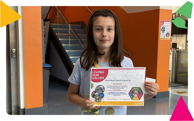 A young girl smiling, holding up a certificate as a values award winner